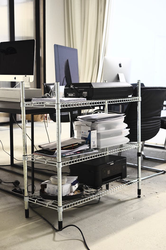 Iron shelves with hardware placed near table with computers in office in daytime